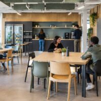 Espace repas de bureau aménagé avec tables, réfrigérateur et micro-ondes
