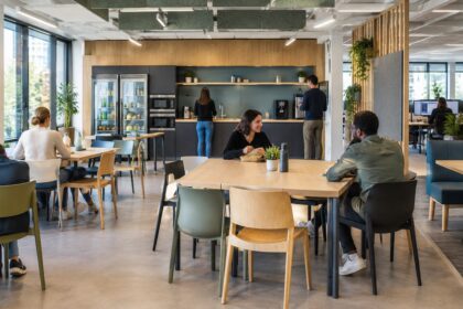 Espace repas de bureau aménagé avec tables, réfrigérateur et micro-ondes